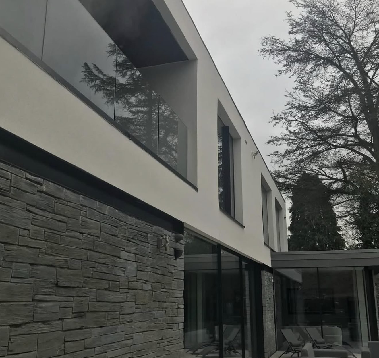Modern house with white render above dark stone cladding and a glass balcony