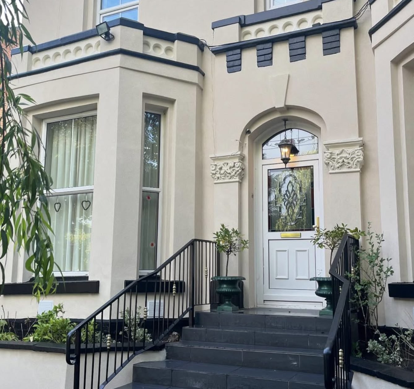Period house front with a cream rendered bay, decorative door surround and iron railings