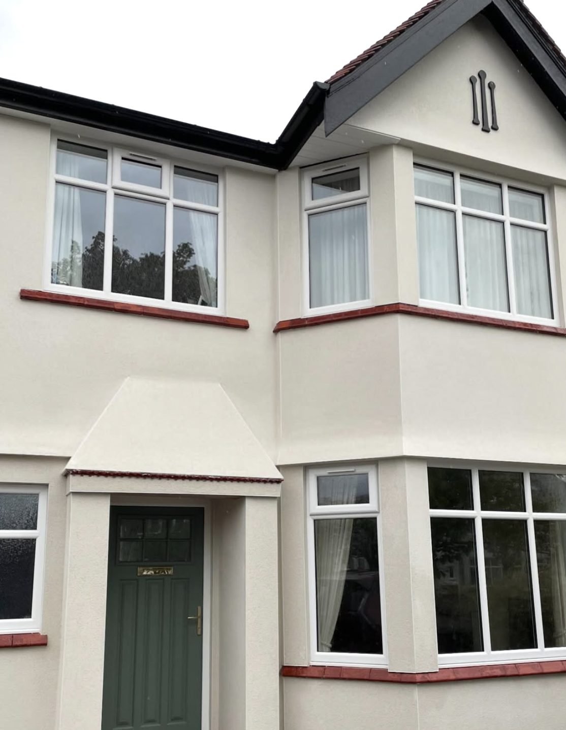 Semi-detached house with curved bay windows in cream render and red tile sills
