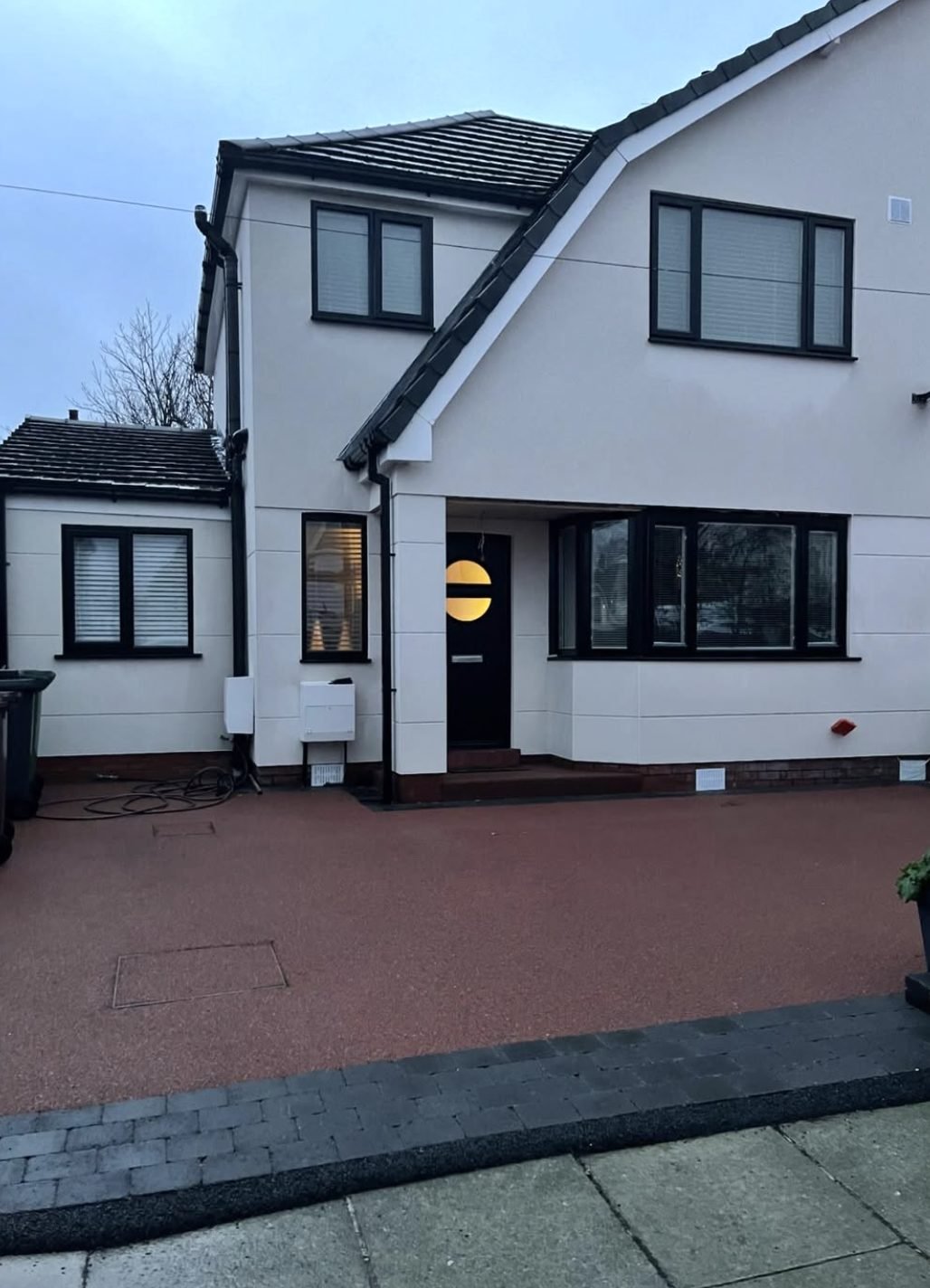 House in white render with black window frames and a red block drive